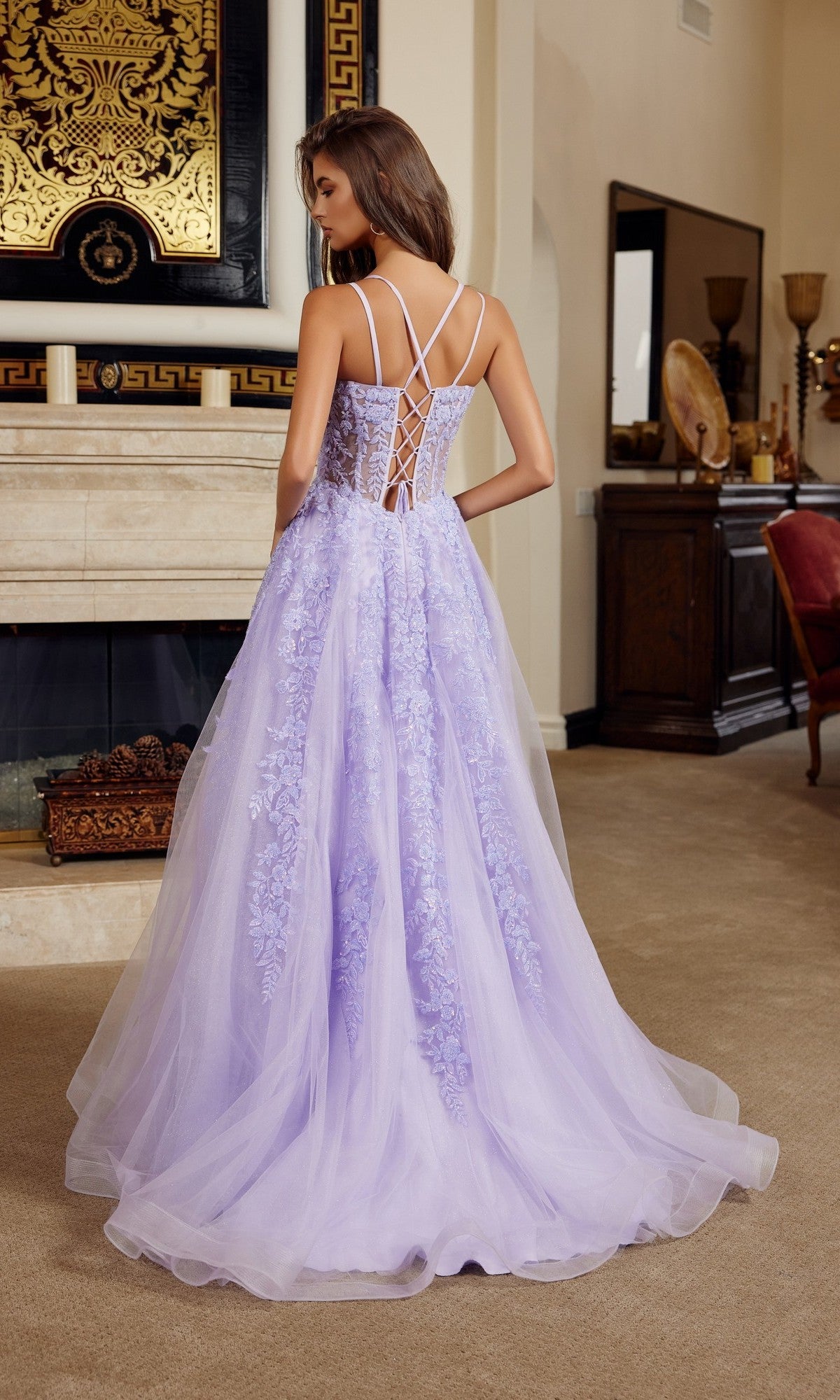 A woman stands indoors facing away from the camera, wearing the Nox Anabel H1882 long prom dress with a lace corset bodice, thin straps, and a pastel tulle A-line skirt.